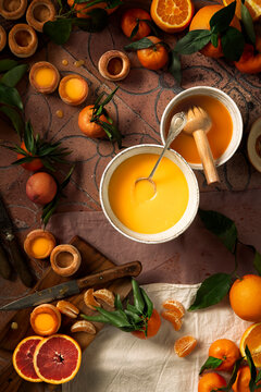 Flat lay of preparation of vol au vent (puff pastries) orange and tangerine mini pies arranged on a cut board and on a textured background, the curd and the juice are placed in two different bowls