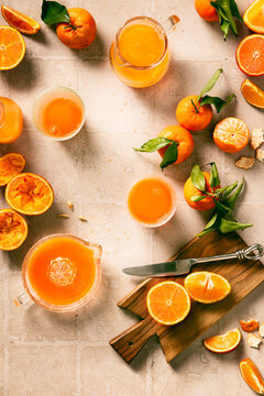 flat lay of blood orange and tangerine juice, in glass bottles and drinking glasses, some oranges just squeezed, some halved.