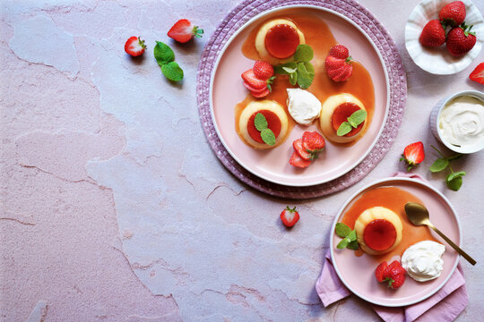 Cr&egrave;me caramel classic French custard dessert topped with a layer of soft caramel sauce and served with strawberries, apple mint and whipped cream. Horizontal with negative copy space.
