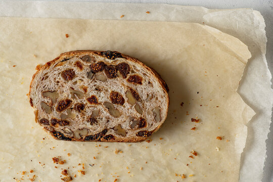 Close-up of a slice of artisanal bread with walnuts and figs, resting on sheets of baking paper.