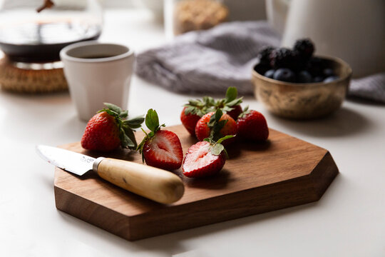 Fresh strawberries on kitchen counter sliced on a wooden board in soft morning light