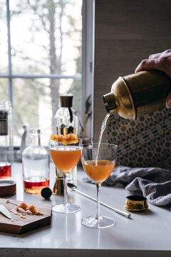 Craft cocktail being poured from a shaker into elegant glasses.