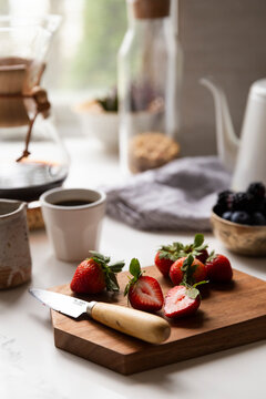 Fresh strawberries on kitchen counter sliced on a wooden board in soft morning light
