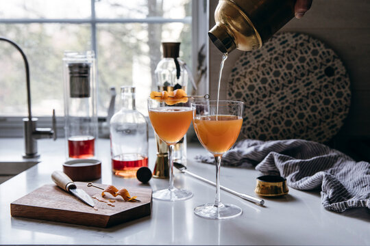 Craft cocktail being poured from a shaker into elegant glasses.