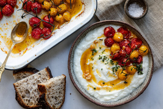 Roasted cherry tomatoes on vine served over creamy yogurt with herbs
