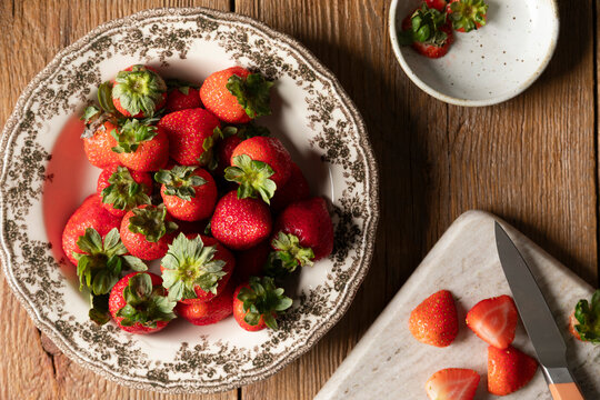 Fresh strawberries in a vintage bowl with sliced berries on a board