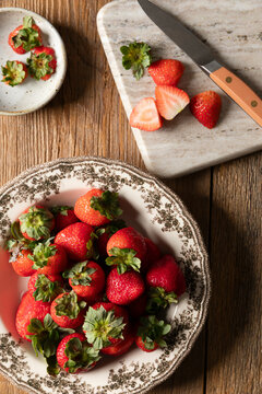 Fresh strawberries in a vintage bowl with sliced berries on a board