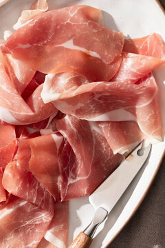 Thin sliced prosciutto on a plate with a small knife