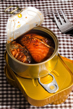 Opened tin of salmon in oil stacked on cans with fork on cloth
