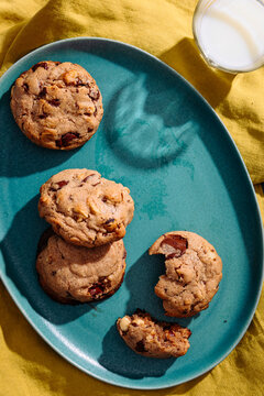 Chocolate chip cookies on teal plate with milk and yellow cloth