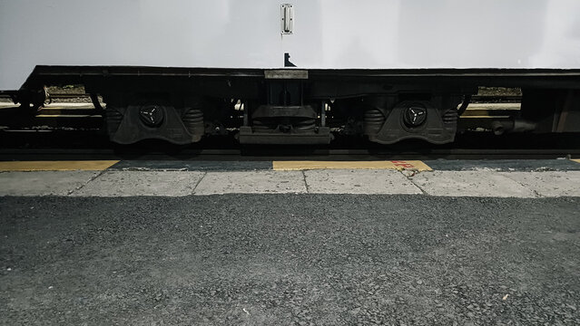 Close up of train wheels and undercarriage at a station platform at night. Side view of a white railway carriage parked on the tracks