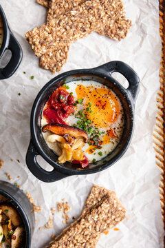 Baked eggs en cocotte with mushrooms, tomatoes, and seed crackers