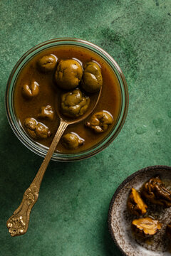 Pickled baby green mangoes in brine with a spoon on green surface