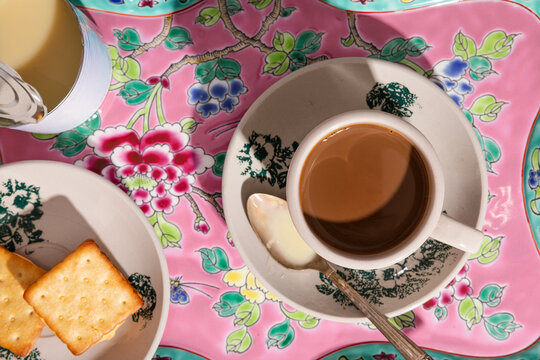 Kopi with condensed milk and crackers on a vibrant floral tray