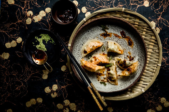 Steamed dumplings with chili oil on speckled plate and woven tray
