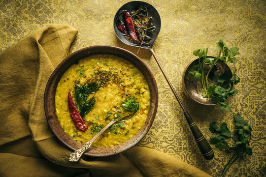Dhal topped with spices, chilies, and herbs on ornate patterned surface