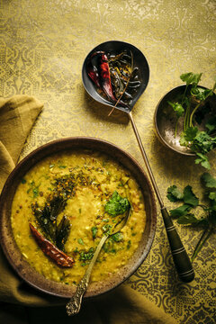 Dhal topped with spices, chilies, and herbs on ornate patterned surface