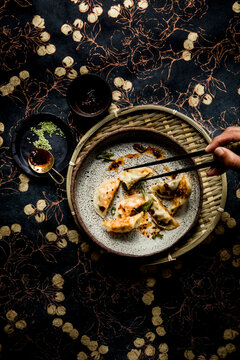 Steamed dumplings with chili oil on speckled plate and woven tray