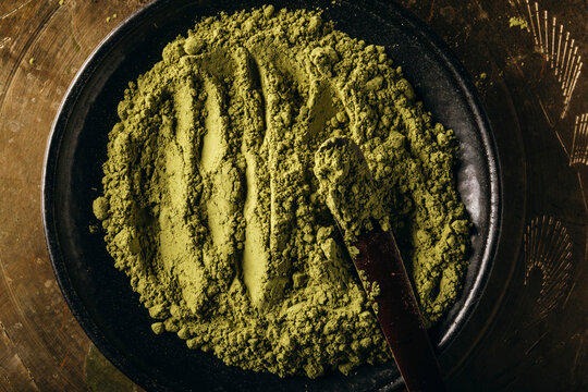 Close-up of matcha powder on a black plate with a wooden scoop