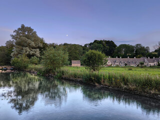 Fototapeta premium The scenic riverside view of river coln with lush green foliage in historic bibury village