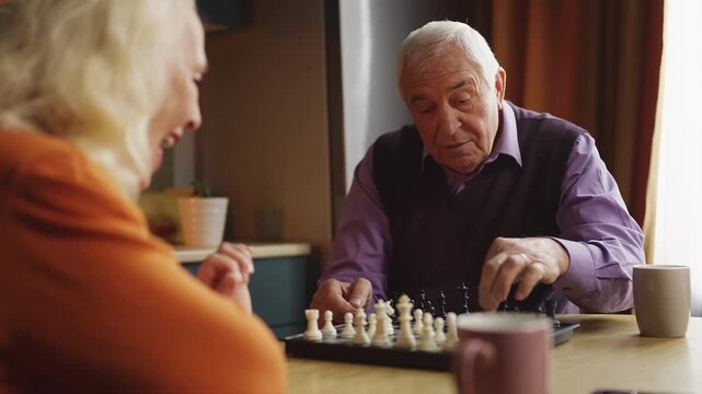 Happy senior man playing chess with smiling wife, enjoying family hobby
