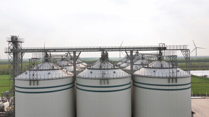 Industrial grain silos and wind turbines standing in the green fields © zhu difeng