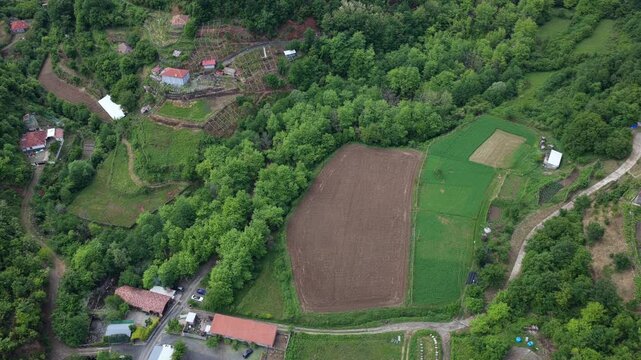 An overhead aerial video of rural homes, backyard gardens, and the dense forest edge of Katund i Vjeter village within the Mirdita Region of Albania.