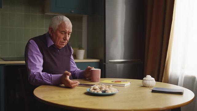 Senior man answering unknown phone call while drinking tea, spam concept
