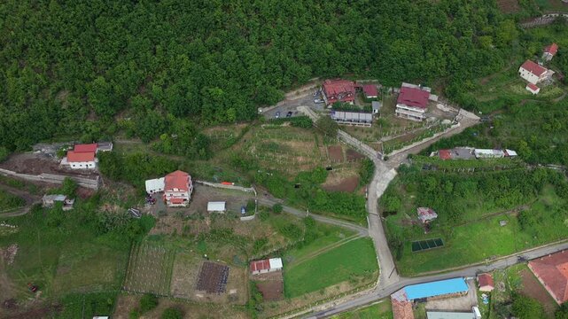 An overhead aerial video of rural homes, backyard gardens, and the dense forest edge of Katund i Vjeter village within the Mirdita Region of Albania.