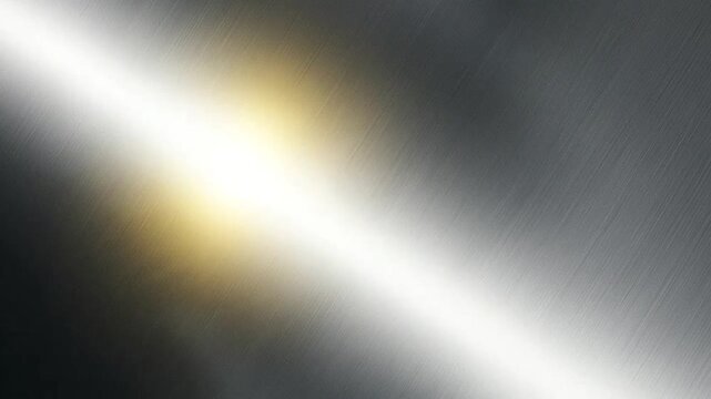 A bright light reflects off a smooth brushed metal surface with diagonal texture lines