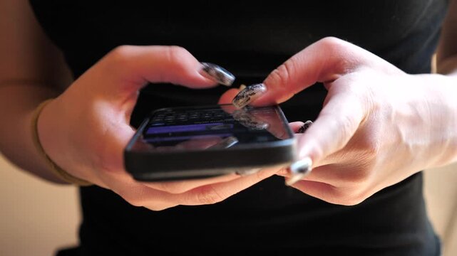 A young woman's hand using a mobile phone, texting, and browsing the internet on her smartphone.