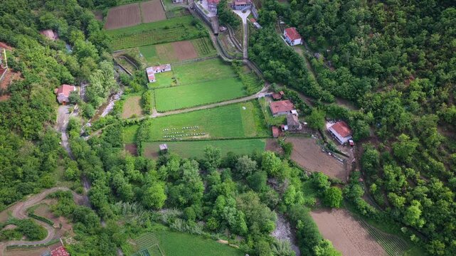 Aerial video capturing cultivated farm fields, rustic buildings, and a narrow river stream in Katund i Vjeter within the Mirdita Region.