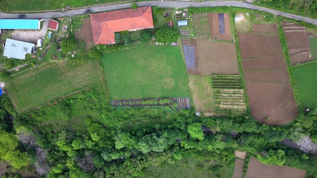 Aerial video capturing cultivated farm fields, rustic buildings, and a narrow river stream in Katund i Vjeter within the Mirdita Region.