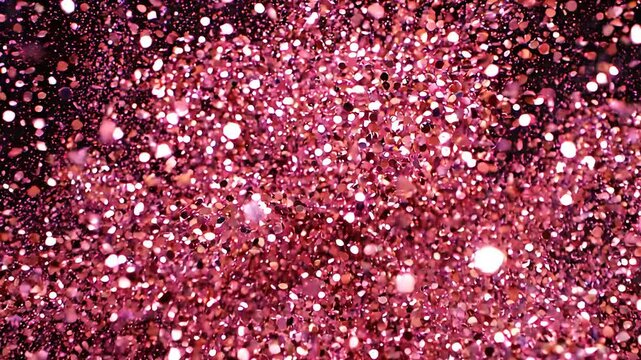 Pink glitter and sequins exploding and shimmering against a black background, slow motion close-up