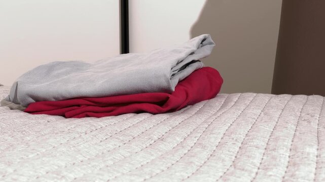 Hands fold clothes on a bed. Neat laundry piles are arranged in a home bedroom. Packing, organizing, and household care concept..