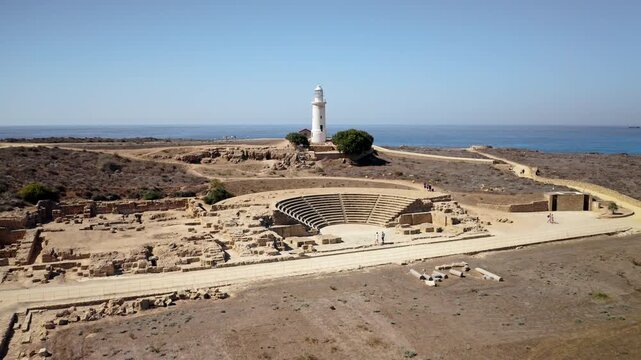 Cyprus, Paphos Lighthouse standing near the ancient Roman Odeon theater amidst archaeological excavations and ruins, overlooking the Mediterranean Sea under a clear blue sky. Aerial view drone flight