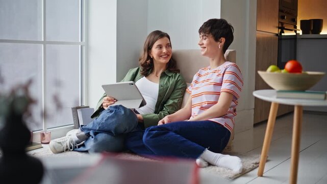 Carefree roommates talking tablet in cozy home. Two women enjoy conversation