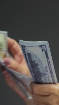 Unrecognizable old mature woman counts cash dollars, holding bundle one hundred dollar banknotes. Arms of senior female holds paper USD money in wrinkled hands after winning lottery bonus. Close up