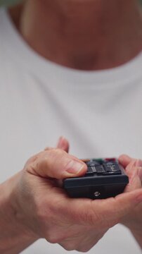 Old woman holds the TV remote control in hands. Senior female presses the button with her finger. Retro viewer presses the buttons on the control panel. Switching channels. Key