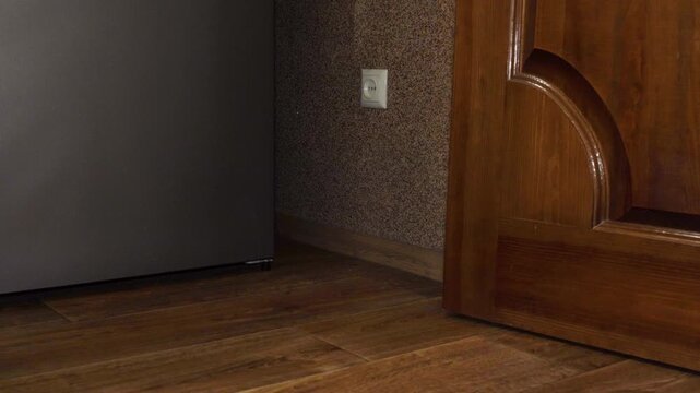 Close-up of feet leaving a room through a classic wooden door, Person in jeans and black sneakers walking out of a wooden door.