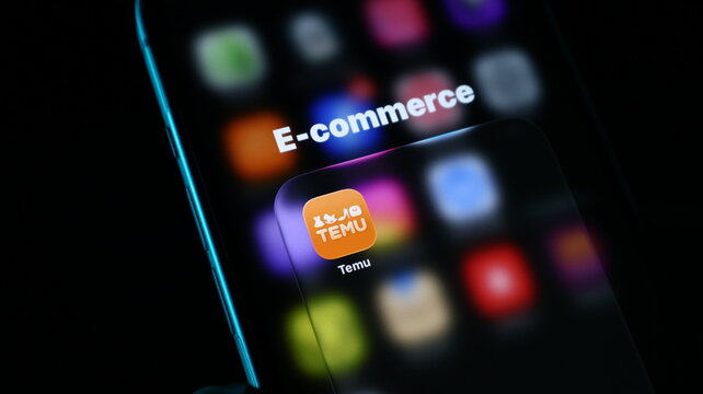 Closeup of a smartphone screen displaying the temu ecommerce app icon with a blurred background of various application icons
