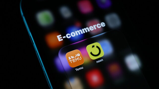 Closeup of a smartphone screen displaying ecommerce app icons including temu and noon, representing online shopping and digital retail