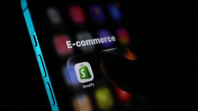 Closeup of a finger touching the shopify app icon on a smartphone screen, representing ecommerce and online business management