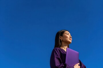 Obraz premium Confident young woman holding a purple folder against a clear blue sky in a calm outdoor portrait