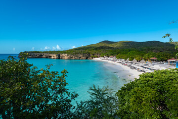 Naklejka premium A stunning view of Grote Knip beach, also known as Kenepa Grandi, in Curacao, showing turquoise waters, white sand, and lush green hills framing the tropical cove.