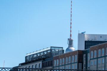 The Berlin TV Tower appears behind layered rooftops and modern city blocks. The clear sky and distant landmark create a compact urban skyline image. © Jakob