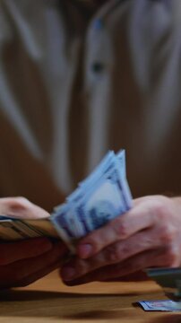 Man investor counting US Dollar bills, close-up. Male trader holds bundle of money, Considers USD at home, evening. Make payment, or have loan. Person manages budget. Hundred paper money cash.