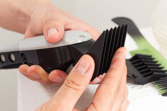 Manual installation of a guide comb on a hair clipper alongside some barbering tools against a light background