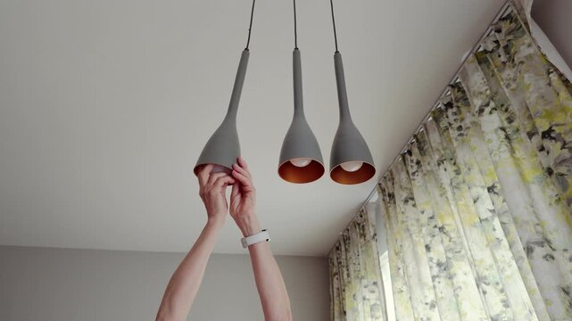 Senior woman installing light bulb into hanging lamp
