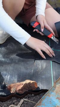 Gardener cutting weed control fabric in garden